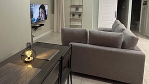 A modern living room with a sofa, a TV, a dining table with chairs, and a ceiling light. - Spacious, cool, and tastefully decorated one bedroom with pull out sofa. (Kingston)