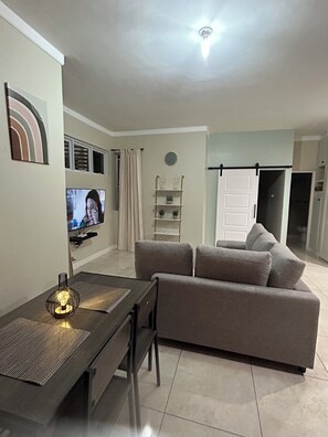 Ein modernes Wohnzimmer mit einer Couch, einem Fernseher, einem Esstisch mit Stühlen und einer Deckenleuchte.