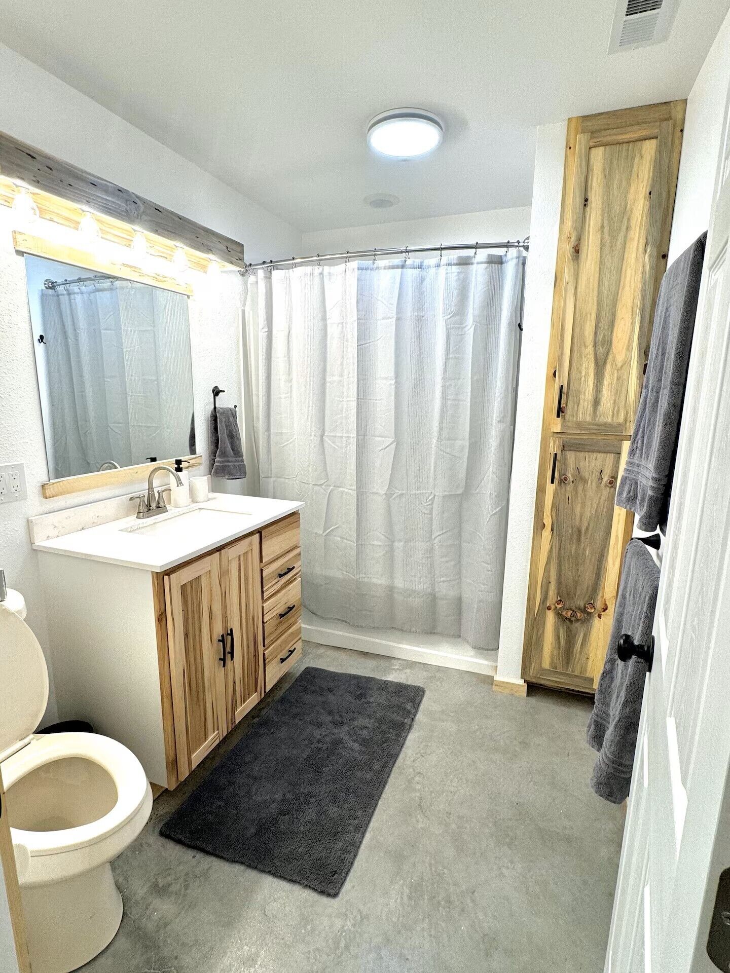 A bathroom with a toilet, sink, mirror, wooden cabinet, shower curtain, and a towel rack.