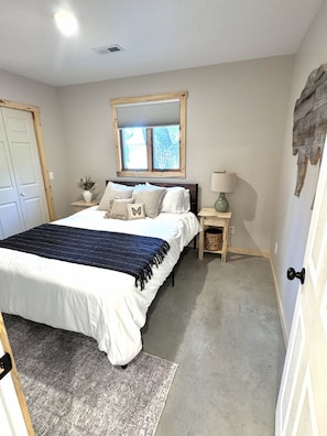 Ein Schlafzimmer mit Bett, Nachttischen, einem Fenster und einer Tür.