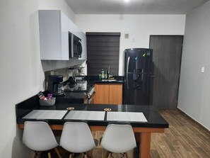 Une cuisine compacte équipée d’un four à micro-ondes, d’une cuisinière, d’un réfrigérateur et d’un petit coin repas avec trois chaises.