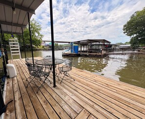 A wooden deck with outdoor furniture, a covered area, and a view of a water body with a dock and buildings in the background.