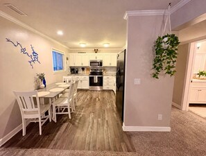 A modern kitchen with white cabinets, stainless steel appliances, and a dining area with a wooden table and chairs.
