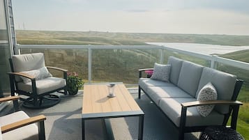 Un balcon aménagé avec un canapé, des fauteuils, une table basse et une vue sur la campagne.