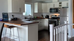 Una cucina moderna con mobili bianchi, un'isola in legno, elettrodomestici in acciaio inossidabile e soffitto in legno.
