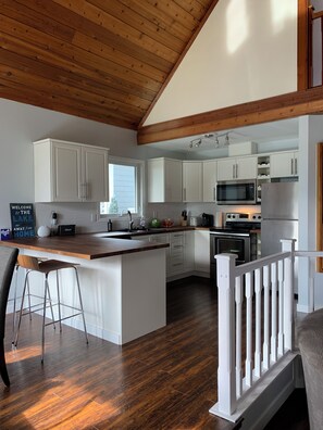 A modern kitchen with white cabinets, a wooden island, stainless steel appliances, and a wooden ceiling.