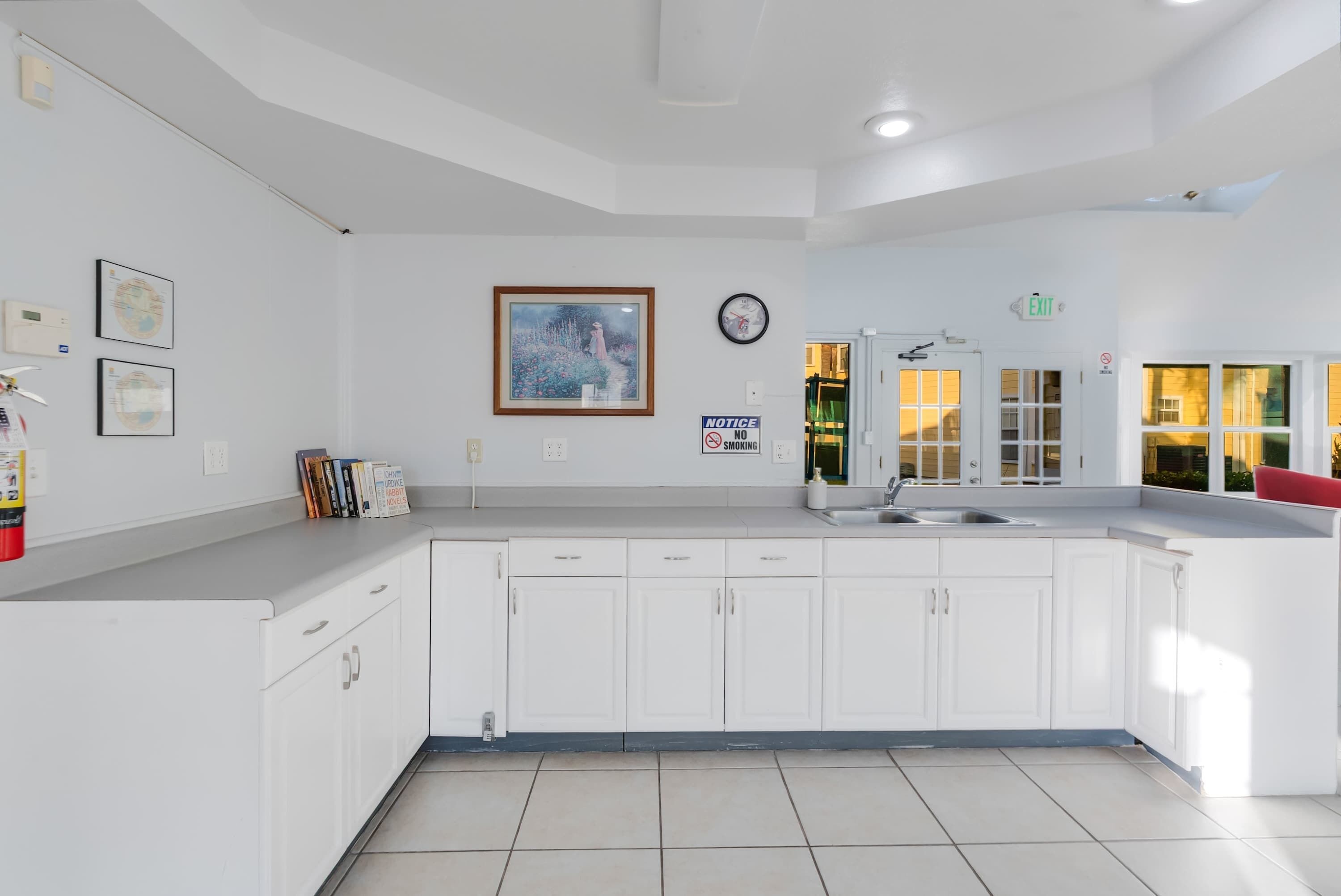A modern kitchen with white cabinets, a sink, and a clock on the wall.
