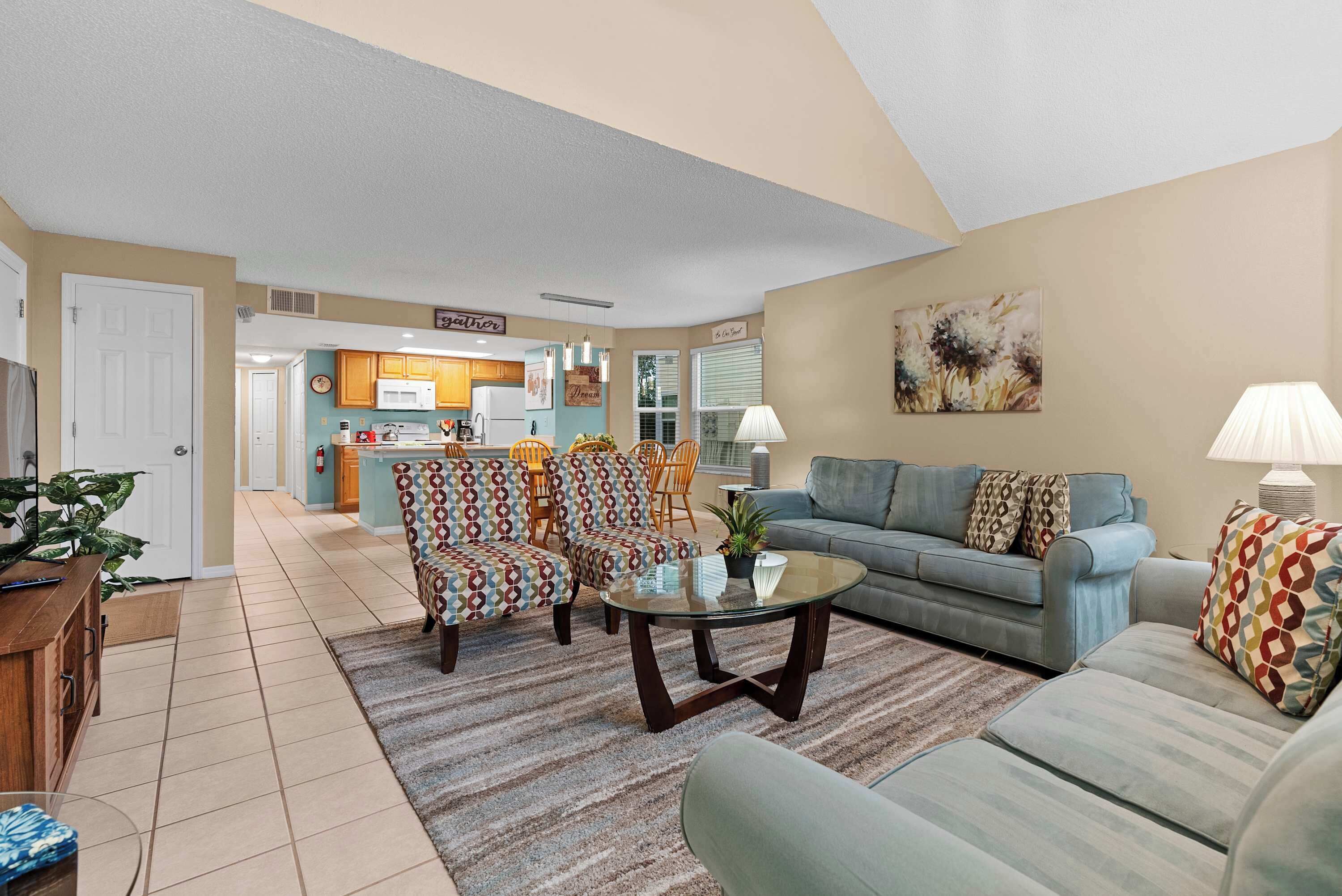A living room with a sofa, armchairs, a coffee table, and a kitchen in the background.