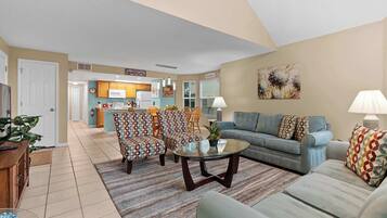 A living room with a sofa, armchairs, a coffee table, and a kitchen in the background.