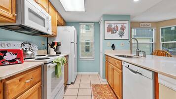 A kitchen with wooden cabinets, a white microwave, a stove, and a dishwasher.