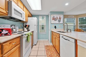 A kitchen with wooden cabinets, a white microwave, a stove, and a dishwasher. - Laguna Bay Family Vacation Retreat (Kissimmee)