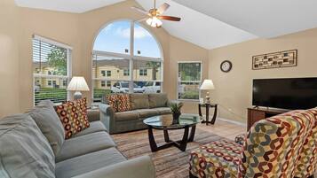A living room with a sofa, ottoman, coffee table, TV, and ceiling fan.
