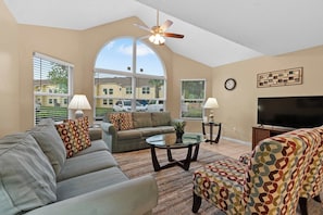 A living room with a sofa, ottoman, coffee table, TV, and ceiling fan. - Laguna Bay Family Vacation Retreat (Kissimmee)