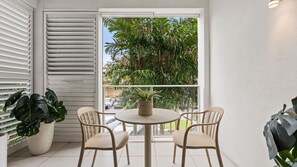 Ein Balkon mit rundem Tisch, zwei Stühlen, einem Blumentopf und Blick auf Palmen und parkende Autos.