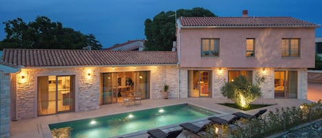 A two-story house with a swimming pool, outdoor seating, and a stone facade.