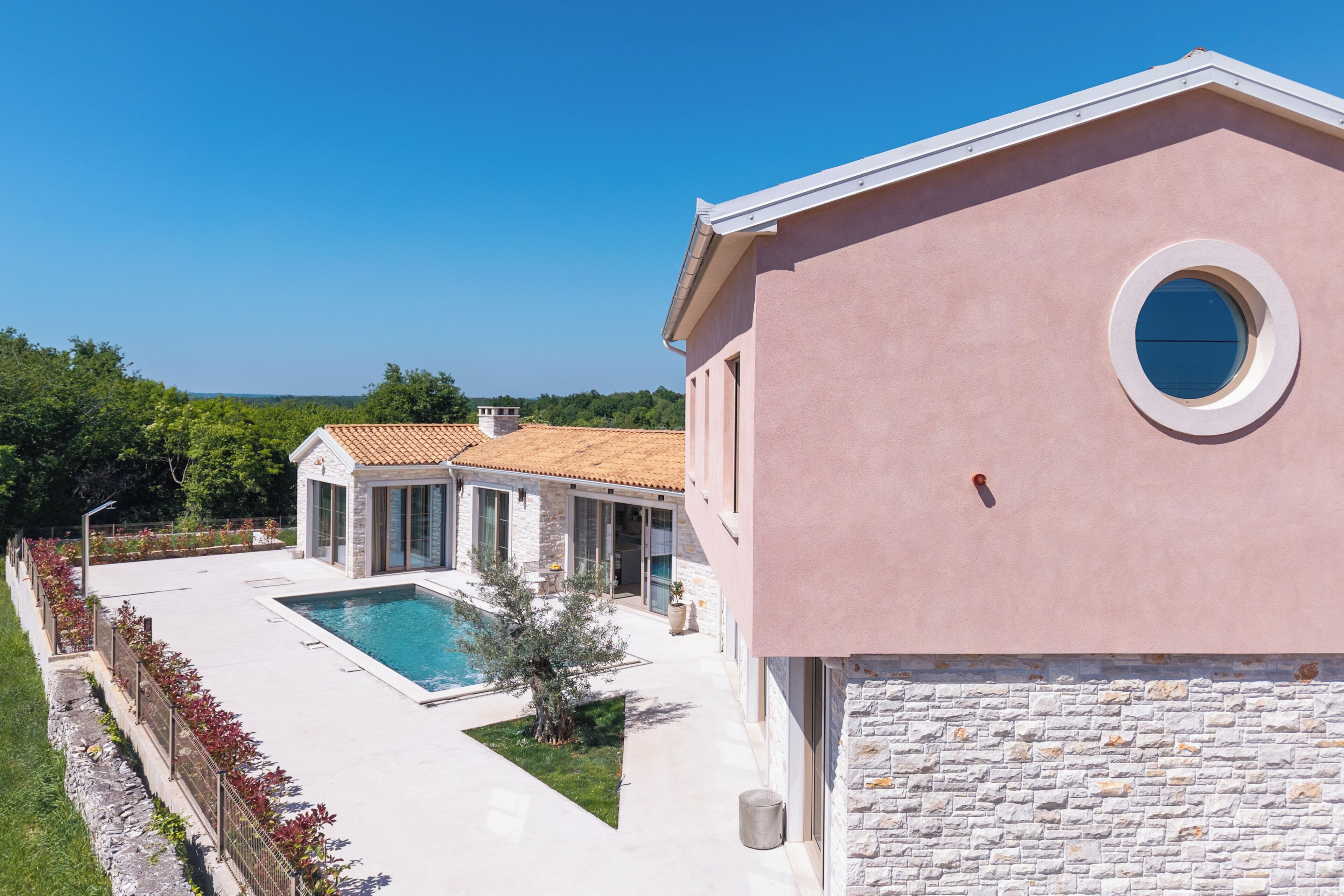 A modern building with a swimming pool, stone facade, and a clear blue sky.