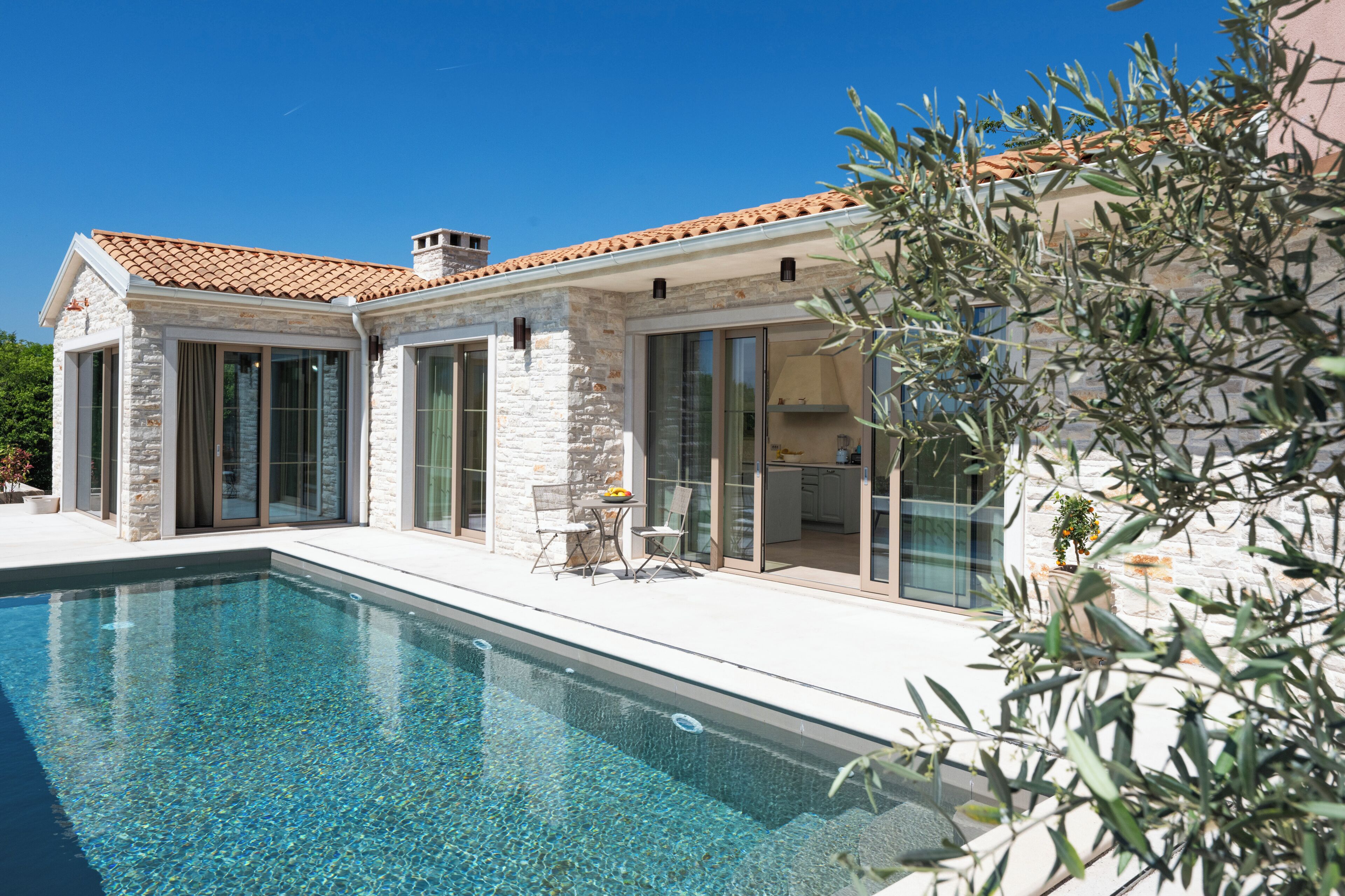 A modern house with a swimming pool, stone exterior, and glass doors leading to a patio area.