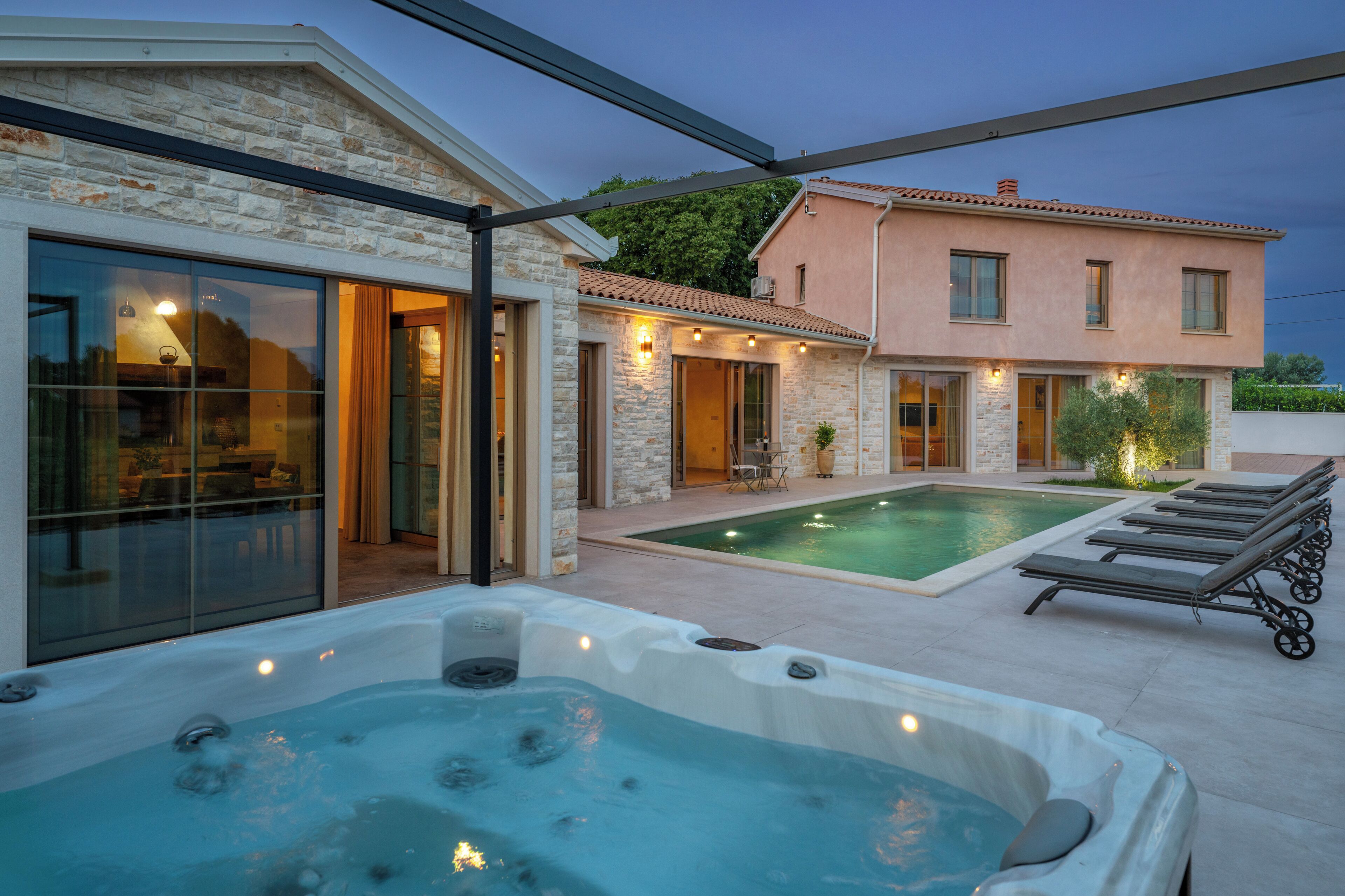 Una casa moderna con piscina, jacuzzi y un patio con sillones de descanso.