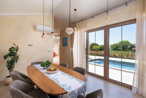 A dining area with a wooden table, grey chairs, a potted plant, and a view of a swimming pool through large glass doors. - Villa Da Ella (Istria - Krnica) (Krnica)