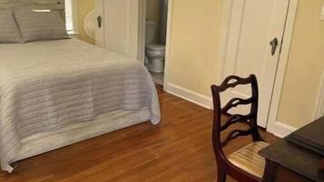 Une chambre à coucher avec un lit, une chaise, une table et une poubelle.