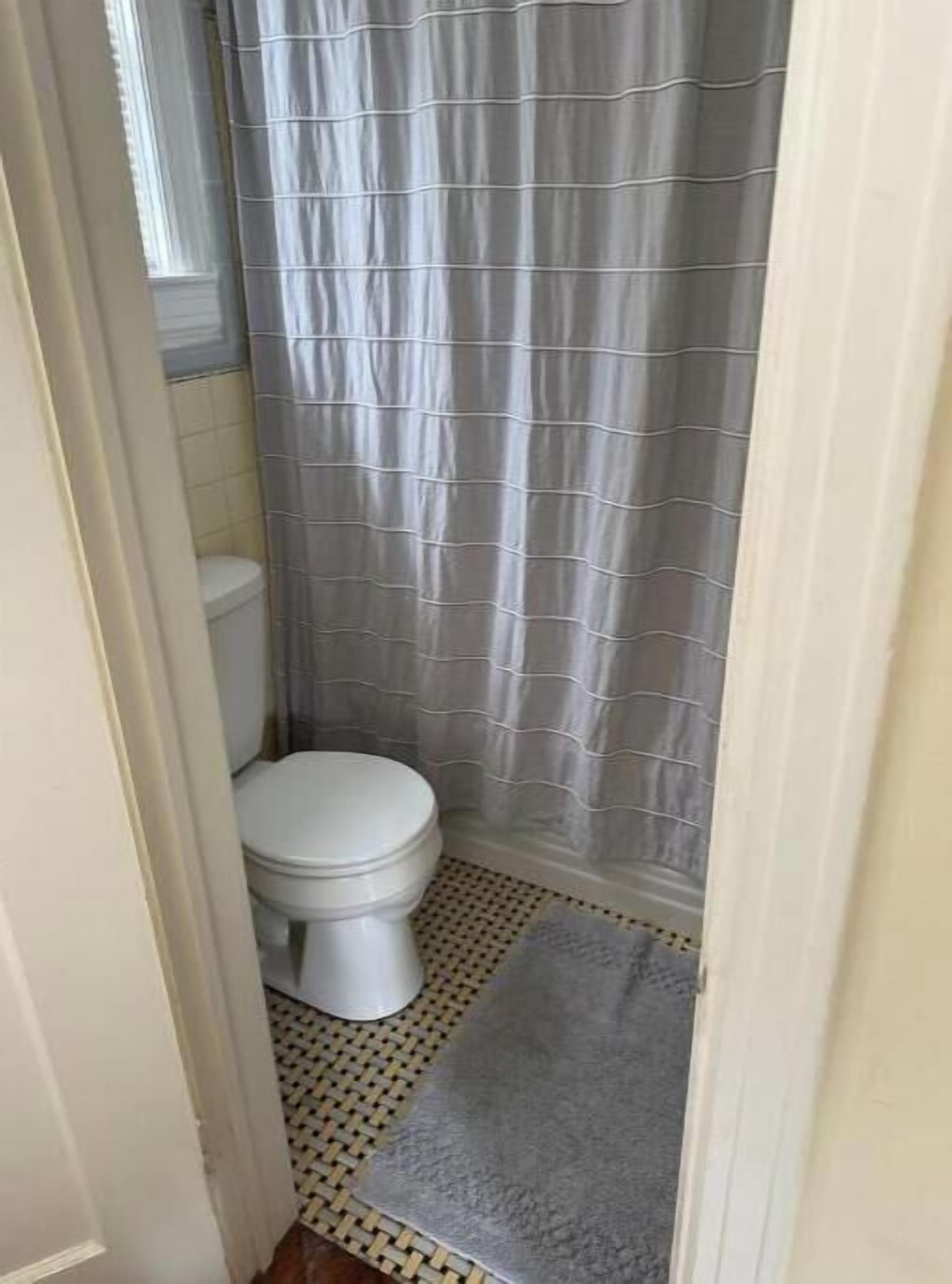 A bathroom with a toilet, a shower curtain, and a patterned floor.