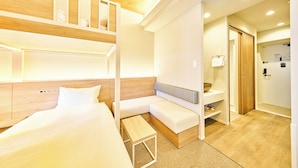 A hotel room with a bunk bed, a sofa, a small table, and a bathroom with a wooden door. - Grand STAY Hakata Nishinakasu (Fukuoka)
