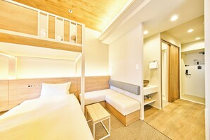 A hotel room with a bunk bed, a sofa, a small table, and a bathroom with a wooden door. - Grand STAY Hakata Nishinakasu (Fukuoka)