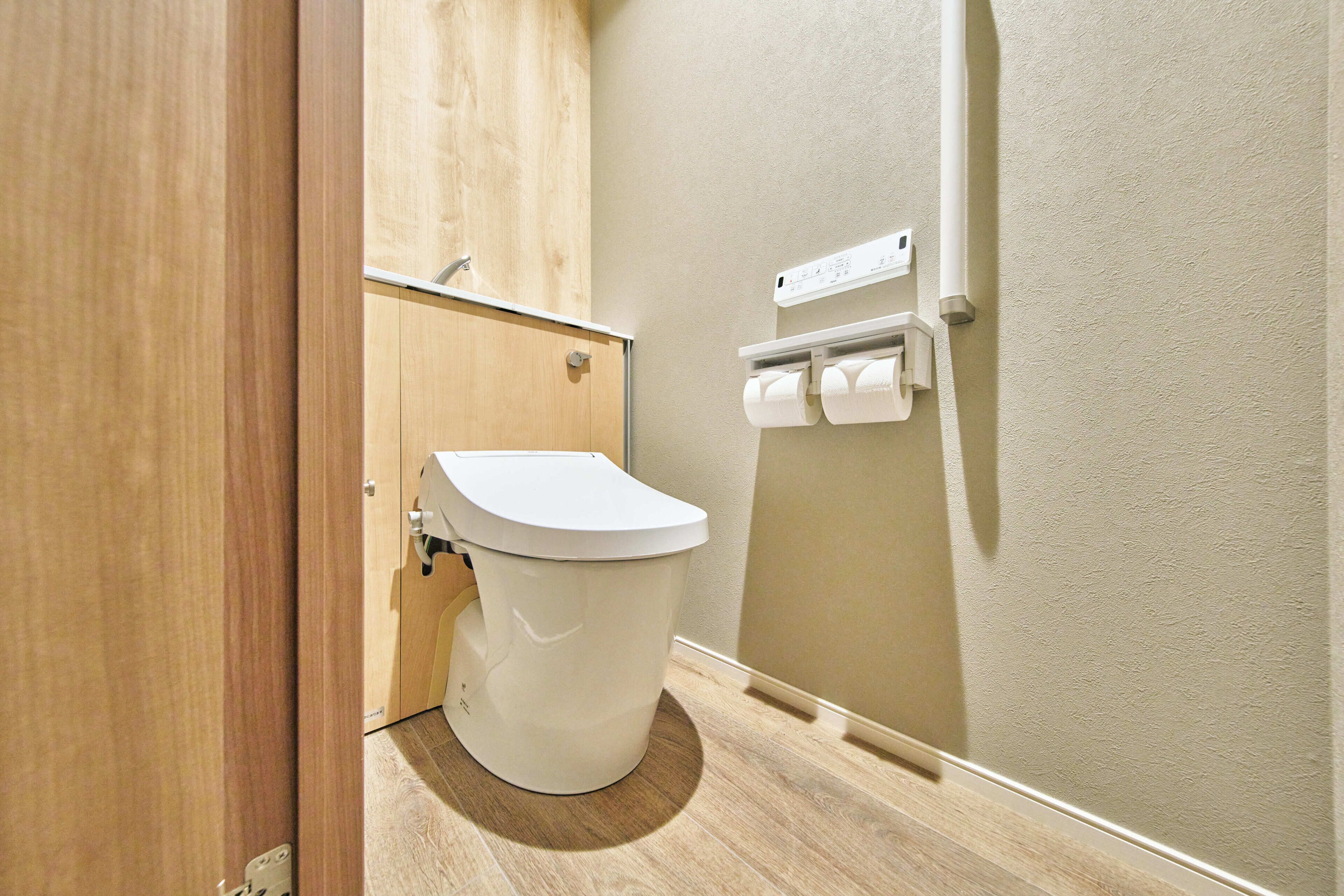 A bathroom with a toilet, wooden cabinet, and toilet paper holder.