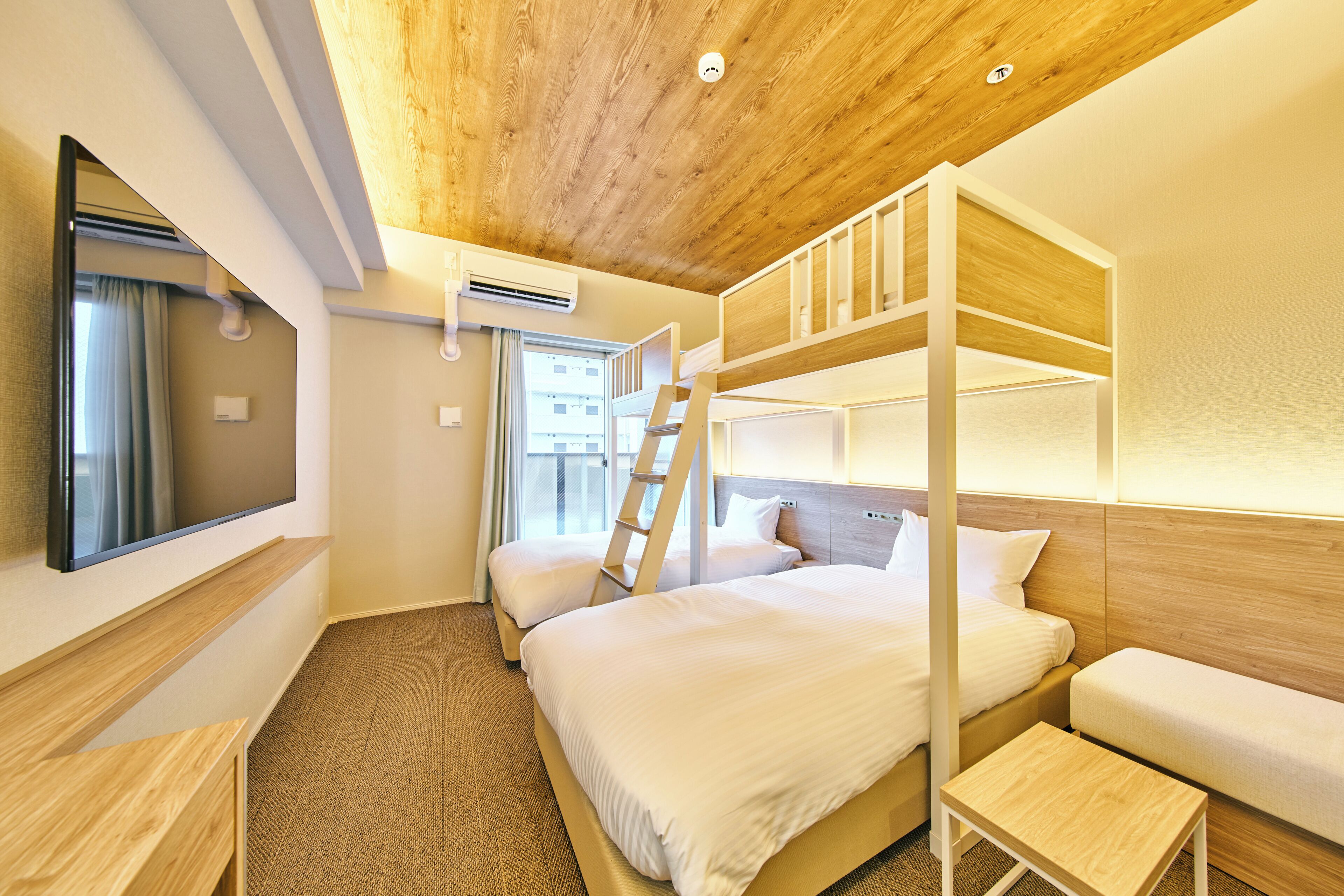Habitación con literas, televisor, una escalera y una mesita.