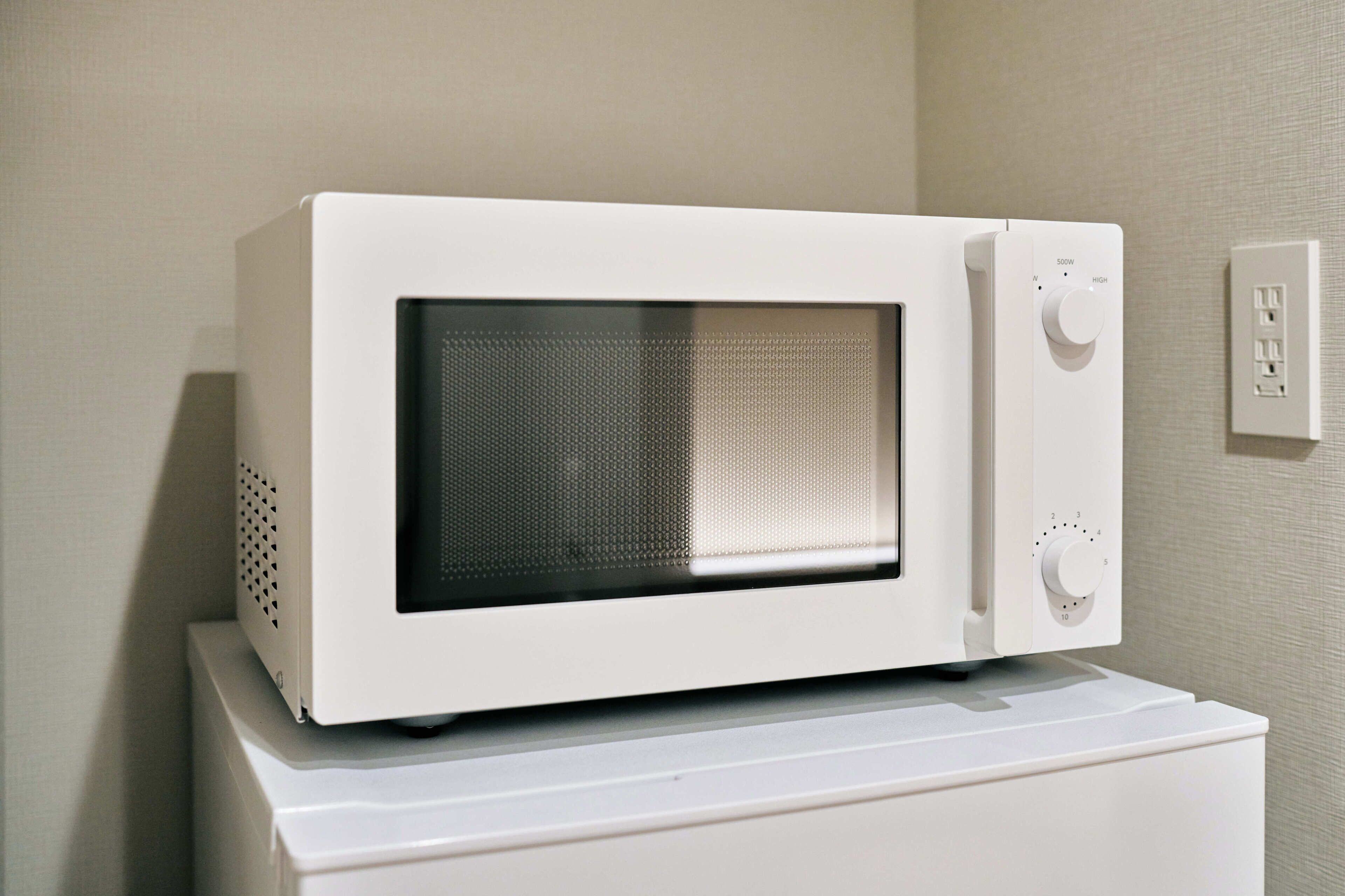Un four à micro-ondes blanc, posé sur un appareil électroménager blanc, avec une prise de courant et un interrupteur sur le mur.
