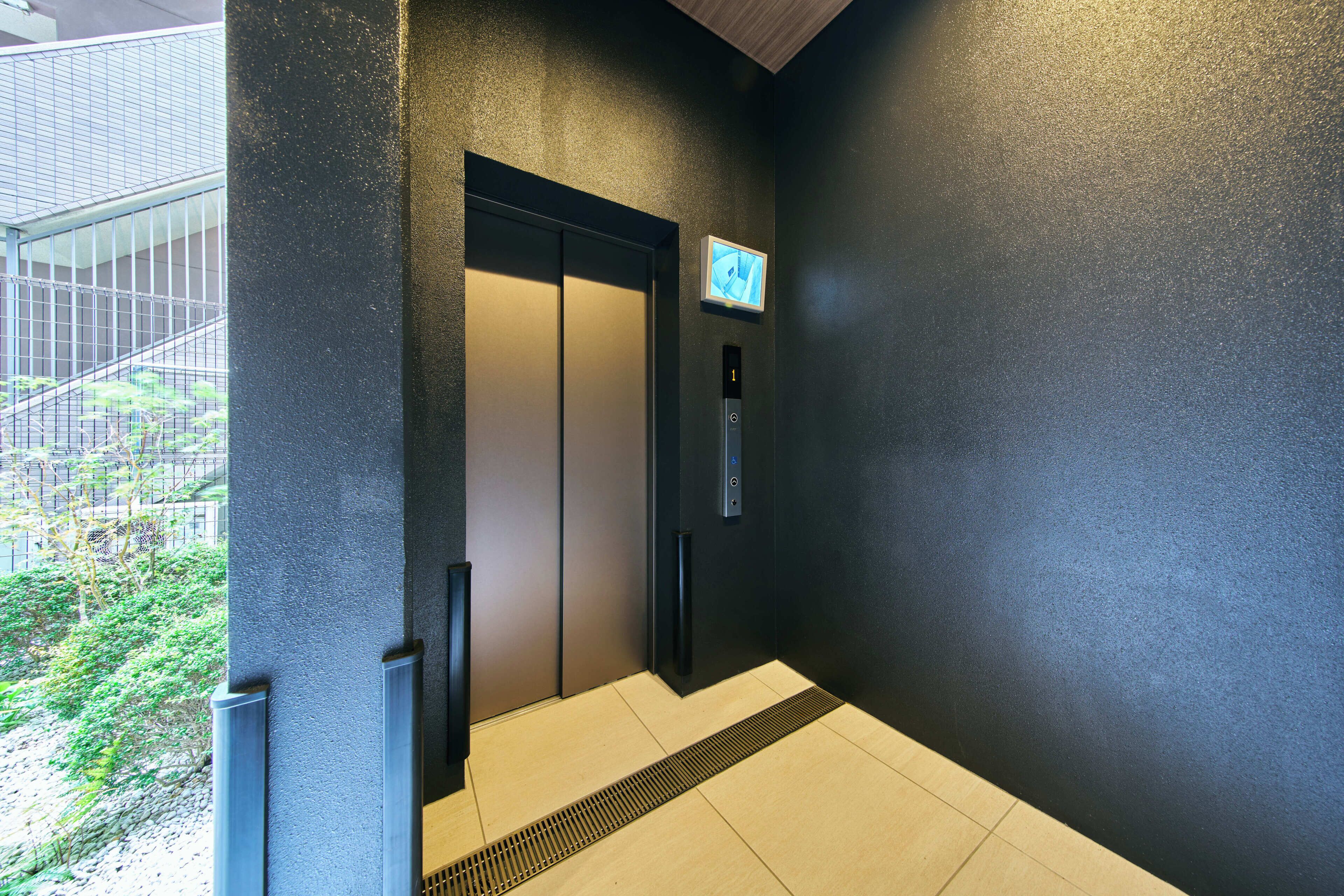A modern elevator with a digital display and a button panel, adjacent to a staircase and a wall with a textured surface.