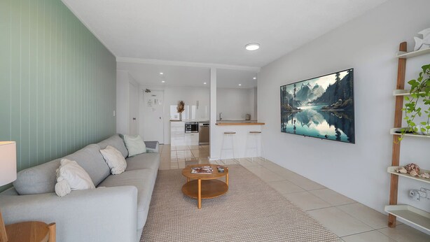 A modern living room with a sofa, coffee table, and a kitchen in the background. - Entire Apartment: Direct Ocean Views, Pool (Kings Beach)