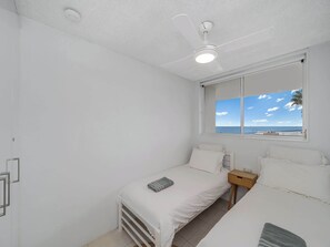 Ein Schlafzimmer mit Deckenventilator, einem Fenster mit Meerblick und einem Bett mit Kissen.