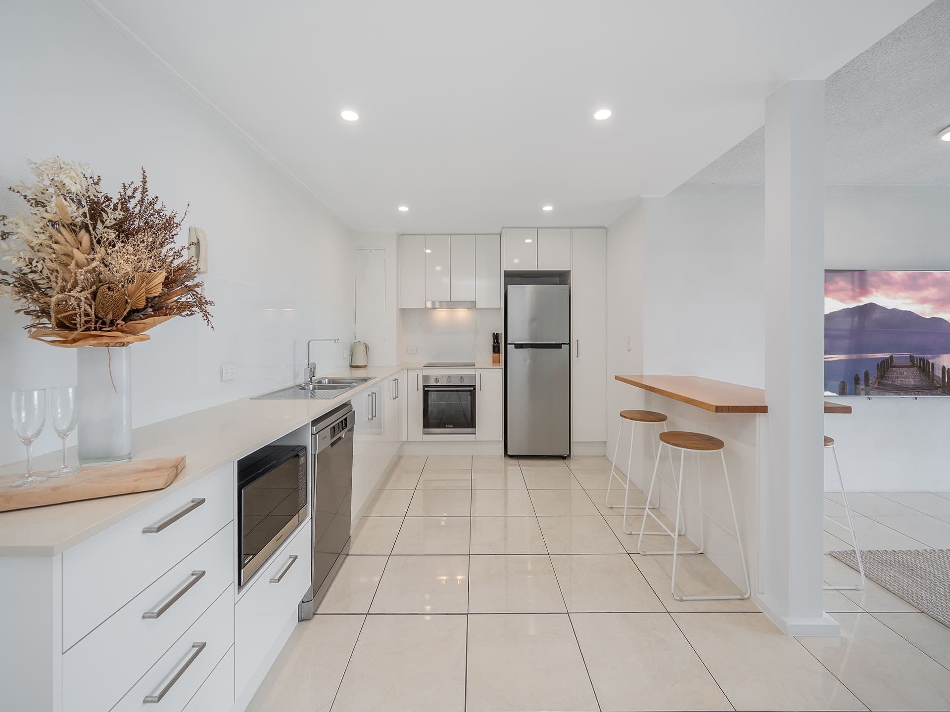 A modern kitchen with white cabinetry, stainless steel appliances, a wooden countertop, and a dining area with stools.