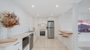A modern kitchen with white cabinetry, stainless steel appliances, a wooden countertop, and a dining area with stools. - Entire Apartment: Direct Ocean Views, Pool (Kings Beach)
