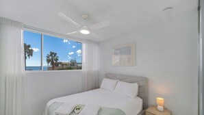 A bedroom with a bed, a nightstand, a ceiling fan, a window with a view, and a framed picture on the wall. - Entire Apartment: Direct Ocean Views, Pool (Kings Beach)