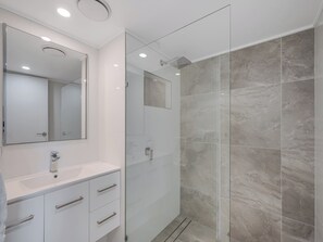 A modern bathroom with a glass shower enclosure, a white vanity with drawers, and a large mirror.