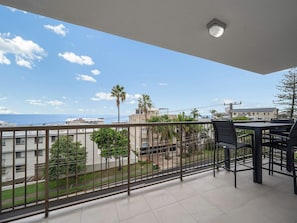 A balcony with a view of the sea, a table with chairs, and a railing.