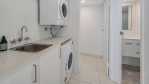 A modern bathroom with a built-in washing machine, a sink with a faucet, and a mirror above the sink. - Entire Apartment: Direct Ocean Views, Pool (Kings Beach)