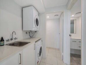 Ein modernes Badezimmer mit integrierter Waschmaschine, einem Waschbecken und einem Spiegel darüber.