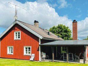 A red barn with a metal roof, a chimney, and a covered porch with outdoor furniture. - 9 Person Holiday Home in Almhult (Almhult)