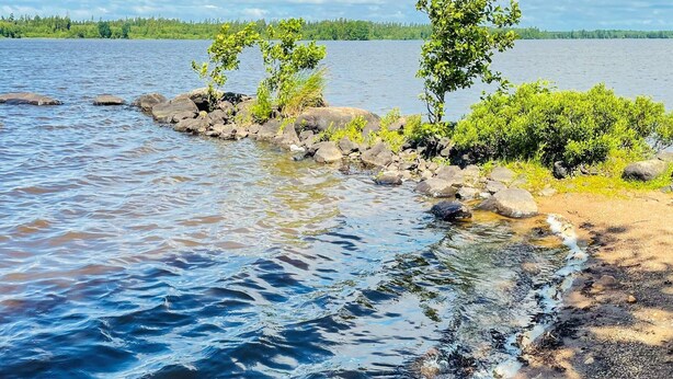 Ein ruhiger See mit klarem Wasser, umgeben von Felsen und Grün.