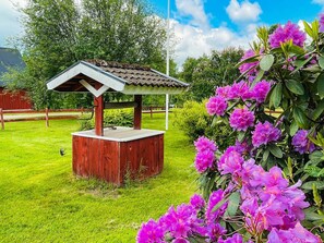 A wooden gazebo with a tiled roof, surrounded by green grass and purple flowers. - 9 Person Holiday Home in Almhult (Almhult)