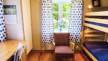 A room with a wooden desk, a chair, a window with polka dot curtains, a bunk bed, and a calendar on the wall.