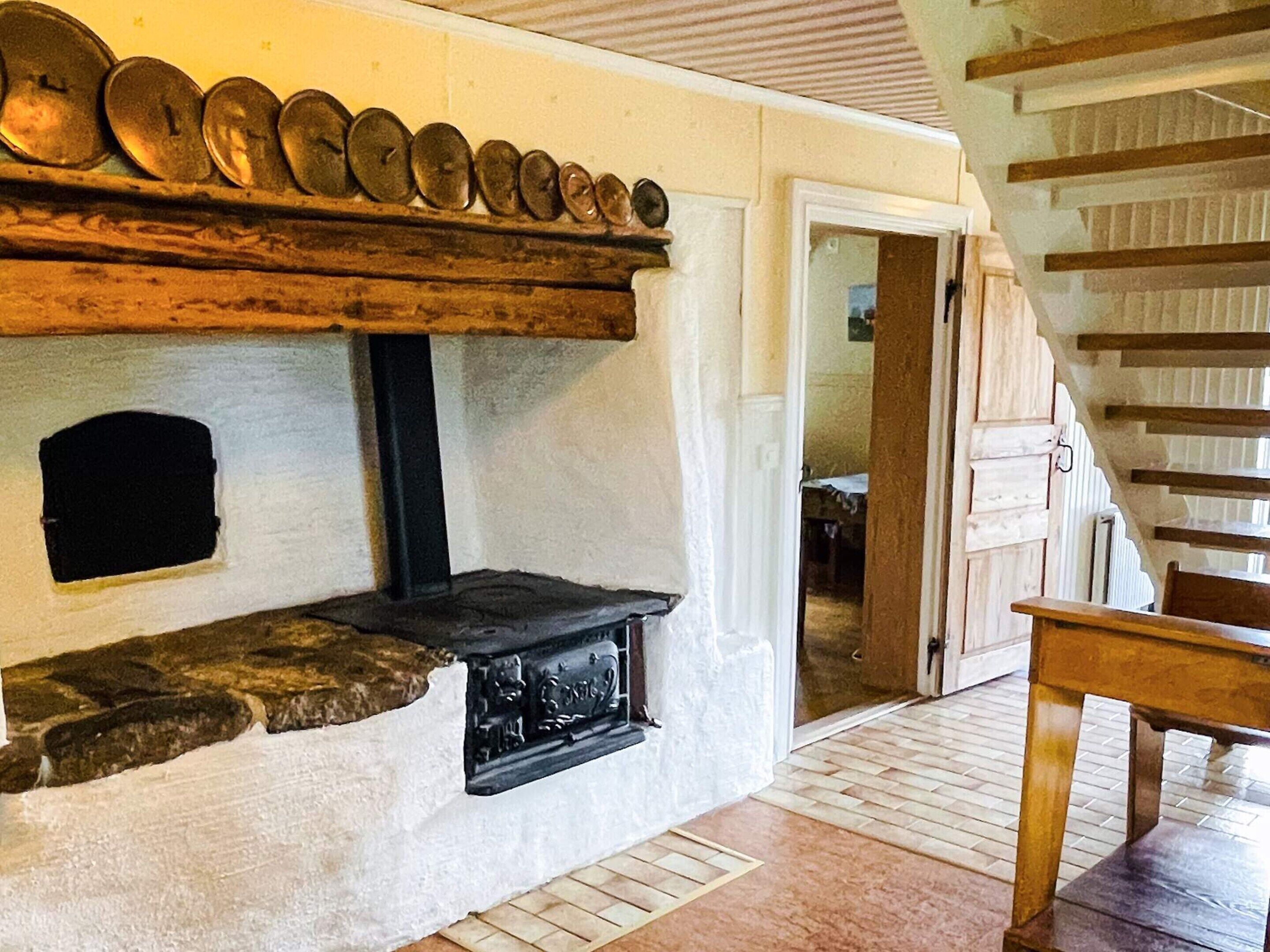 A stone fireplace with a black hearth, a wooden shelf above it, and a wooden staircase to the right.