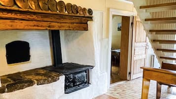 A stone fireplace with a black hearth, a wooden shelf above it, and a wooden staircase to the right.