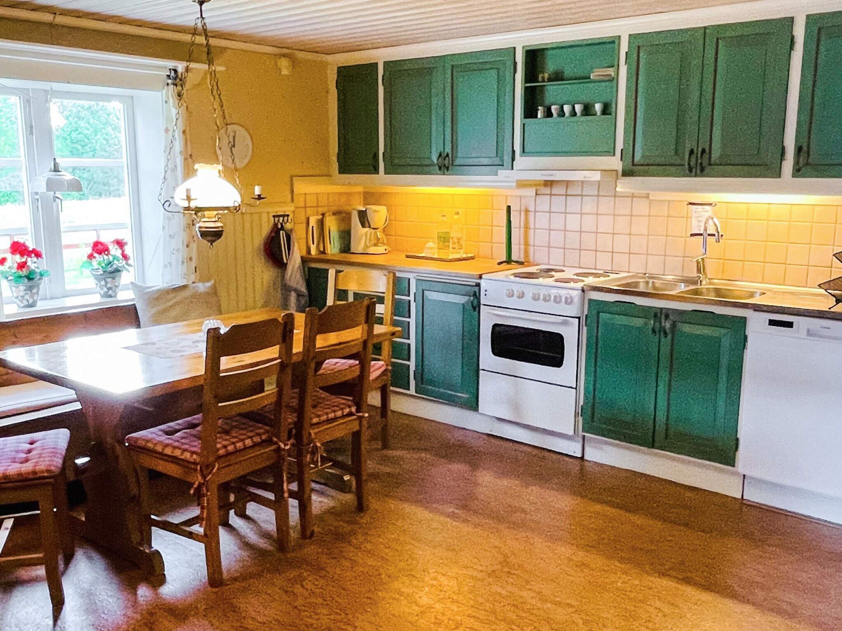 A kitchen with green cabinets, a stove, and a sink. There is a dining table with chairs.