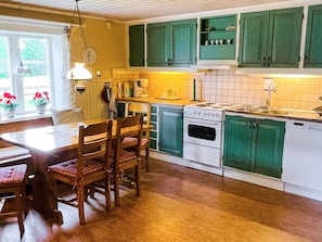 A kitchen with green cabinets, a stove, and a sink. There is a dining table with chairs. - 9 Person Holiday Home in Almhult (Almhult)
