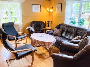 A living room with a brown leather sofa, two armchairs, a small round table, and two wall-mounted lamps. - 9 Person Holiday Home in Almhult (Almhult)