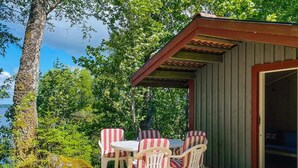 Eine Holzterrasse mit Tisch und Stühlen, einem überdachten Bereich und Blick auf ein Gewässer.